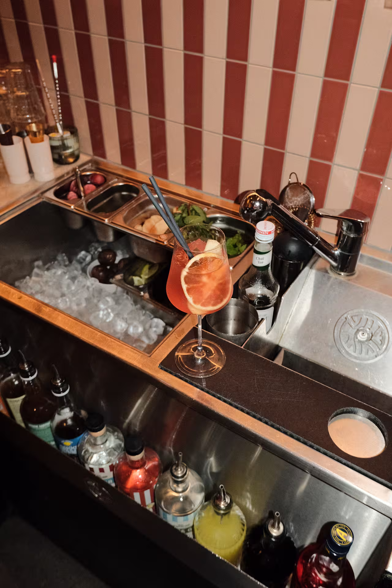 Sjakin Spritz cocktail met bloedsinaasappelschijfje en rietjes op een bar.